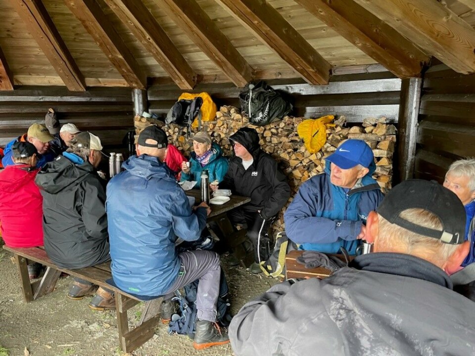 Matpause i gapahuk ved Rørvatnet. Turkledde folk rundt rasteplassbord inne i en stor gapahuk.