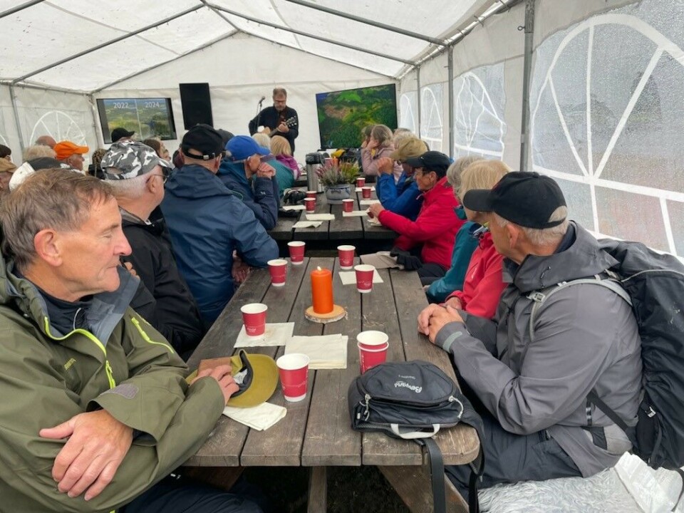 Musikkinnslag ved Karstein Mauset. Mange turkledde folk rundt flere rasteplassbord inne i et partytelt. I bakgrunnen en man som spiller gitar.