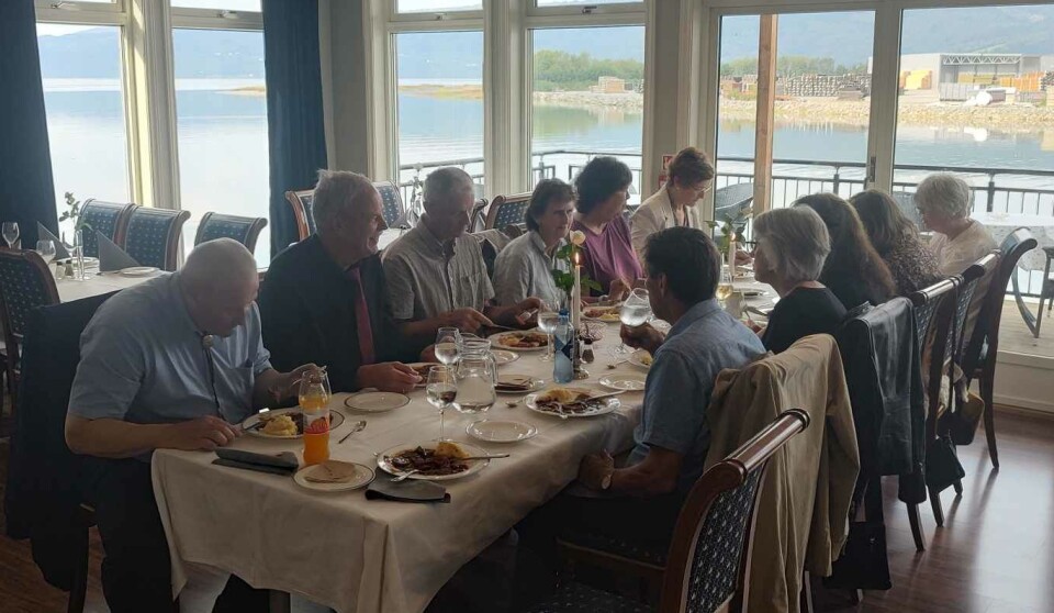 God stemning og god mat på Hammerstuene etter gudstjenesten. Personer rundt et langbord med hvit duk som spiser middag, med utsikt mot surnadalsfjorden.