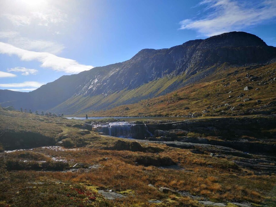 Fjellgruppetur til Vassdalen Ei gruppe turgåere som går på rekke ved et fjellvann. Et fjell i bakgrunnen.