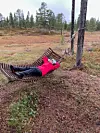 Ei dame som ligger i ei hengekøye av tre, mellom furuer i marka.