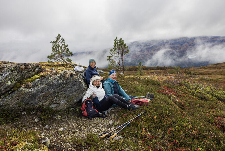Damer som lurte oss med å starte tidlegare. Tre blide turkledde damer som har tatt en rast ved en stor stein på fjellet.