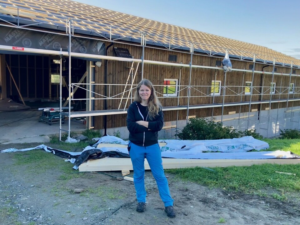 Ingunn Tørset viser stolt frem den nye driftsbygningen som skal stå klar om en drøy måned. Fjøs med trekonstruksjon og brunt panel under oppføring.