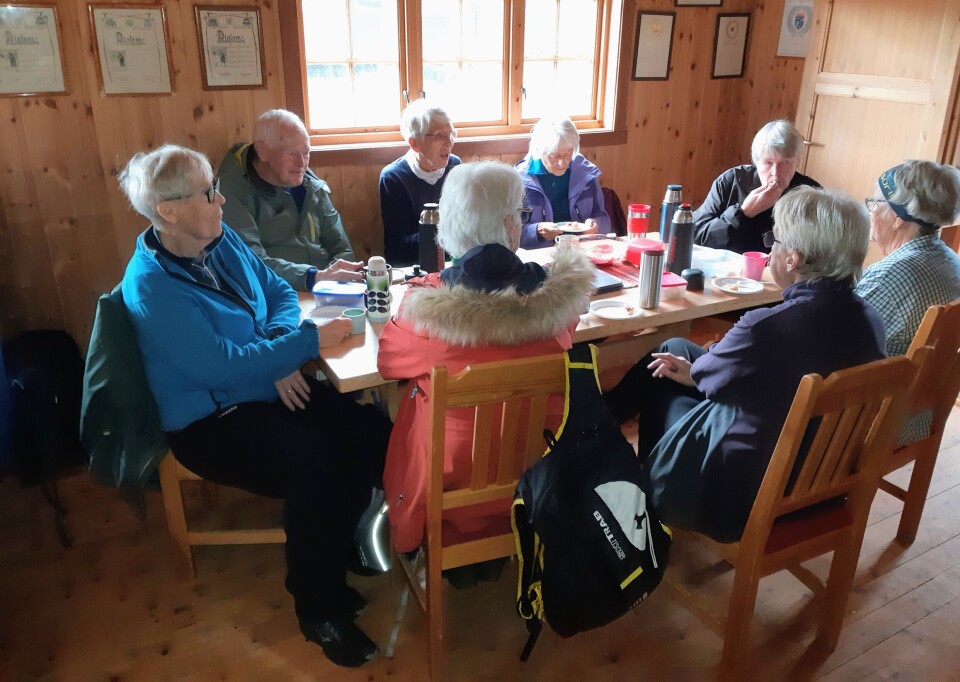 Stavgangtur til Øygardshalsen Flere personer som sitter og spiser niste ved et bord inne i ei hytte.