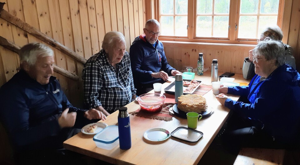 Stavgangtur til Øygardshalsen Flere personer som sitter og spiser niste ved et bord inne i ei hytte.