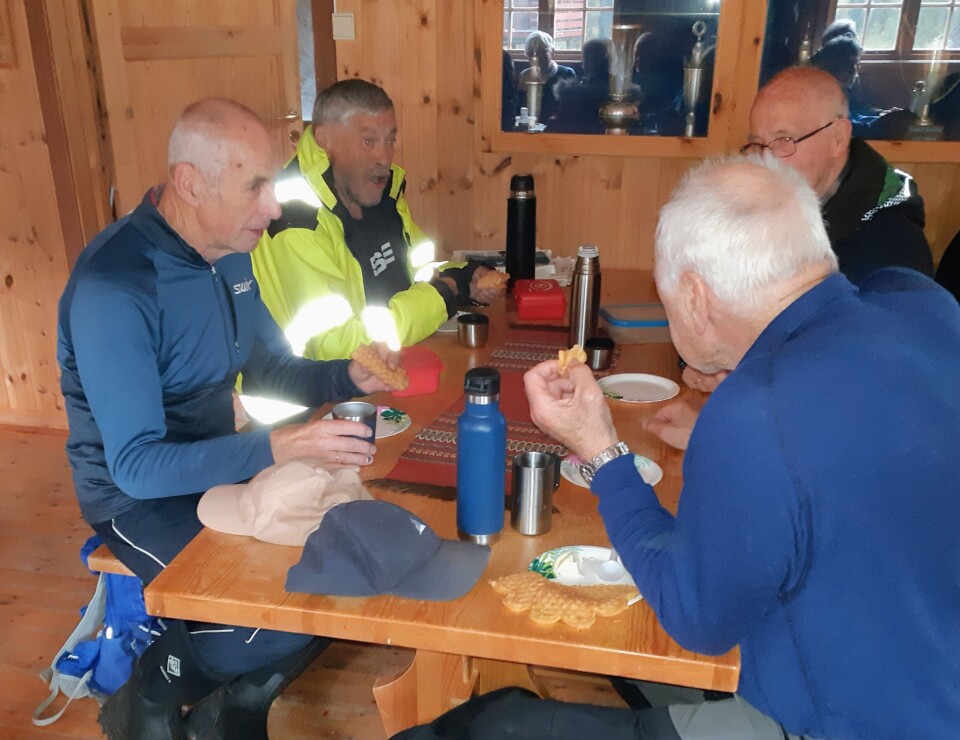 Stavgangtur til Øygardshalsen Fire personer som sitter og spiser niste ved et bord inne i ei hytte.