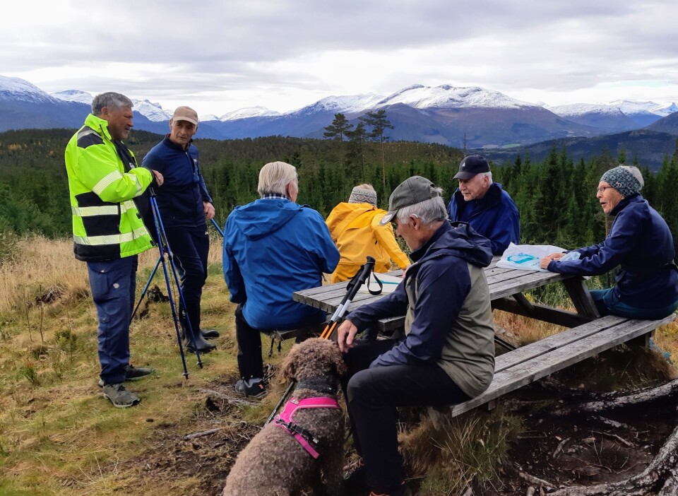Stavgangtur til Øygardshalsen Flere menn som har tatt en rast på en fottur i marka. Noen av dem sitter ved et rasteplassbord. I bakgrunnen er det snø på de høyeste fjelltoppene.