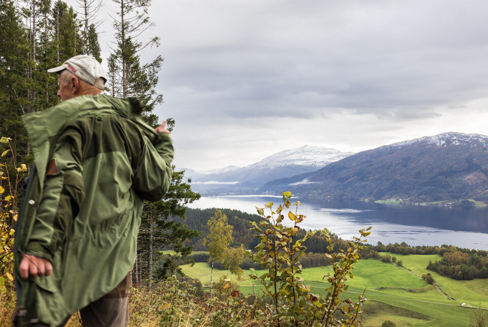 På tide å kaste jakka på Ekjeslia. En turkledd mann som tar av seg jakka. Fjord og fjell i bakgrunnen.