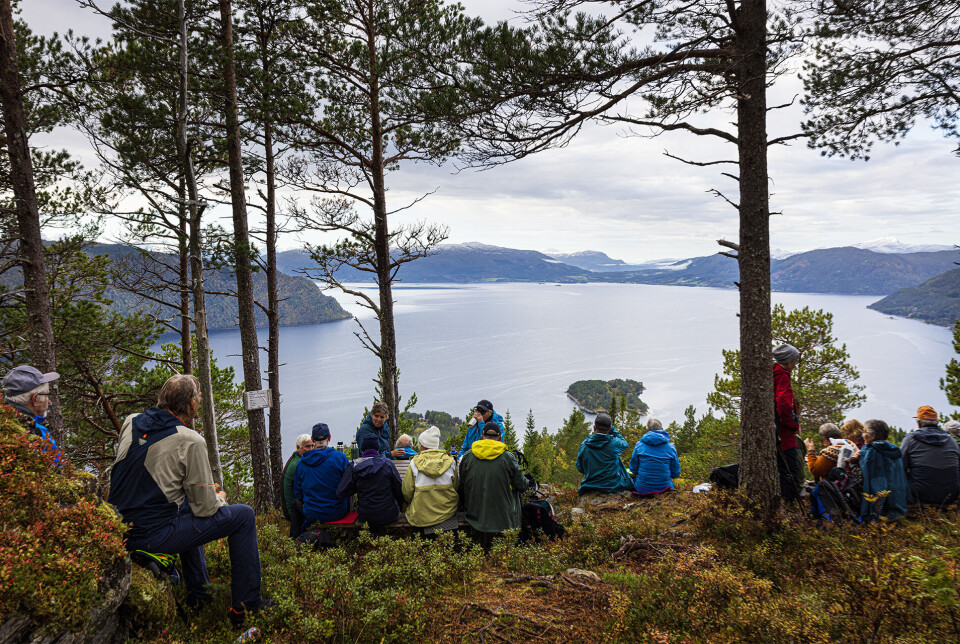 Matpause på Persullukammen. Flere turkledde personer som har satt seg ned i ei li med utsikt mot fjorden.