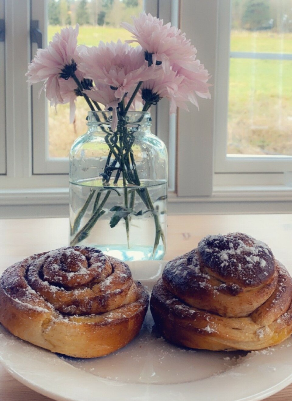 🍁Høstferie-utsalg oppi Lia🍁 En vase med blomster og en tallerken med to kanelsnurrer foran et vindu.