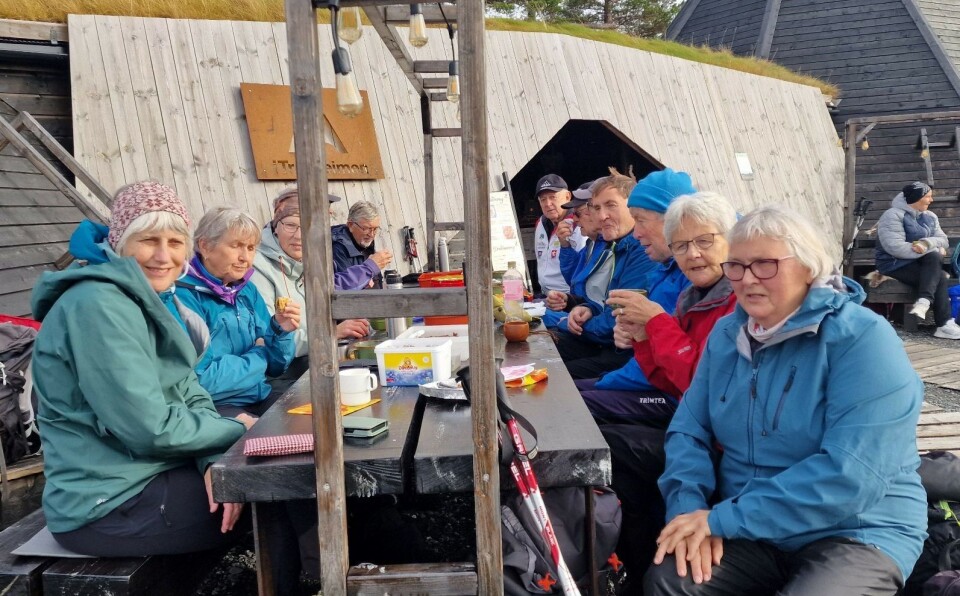 Andre tok matpausen utendørs. Mange turkledde folk som sitter og spiser på et rasteplassbord foran en trebygning.