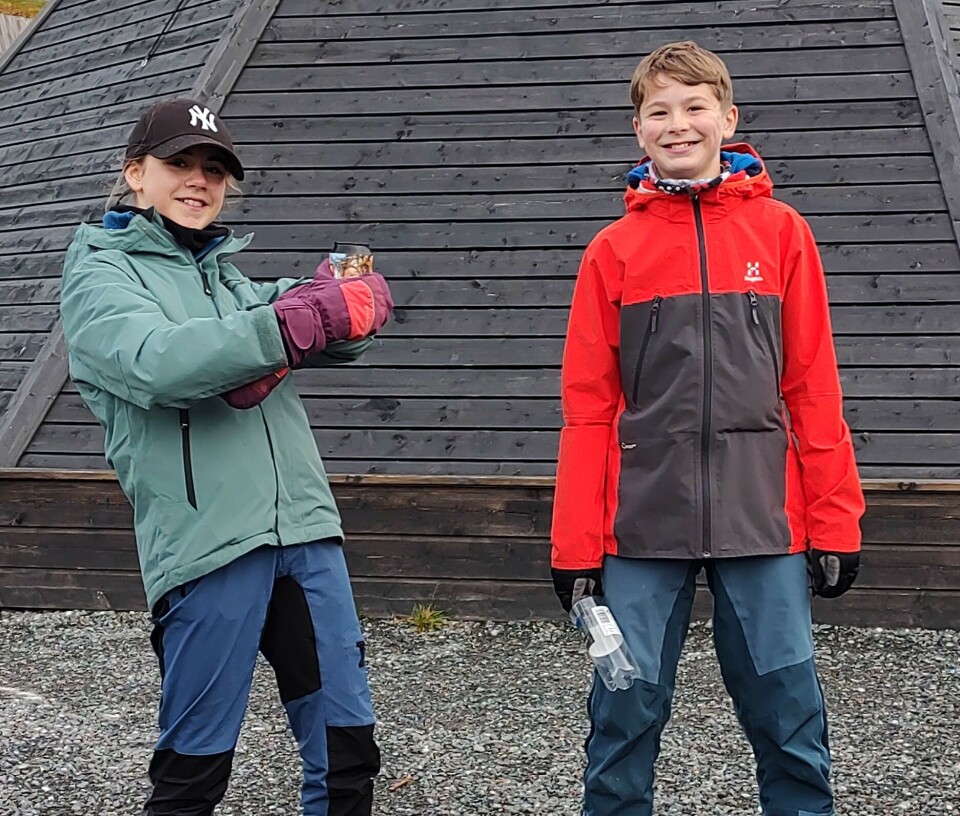 Ronja og Einar. Rekrutter? Ei ung jente og en ung gutt kledd i turklær foran en trebygning. Begge smiler.