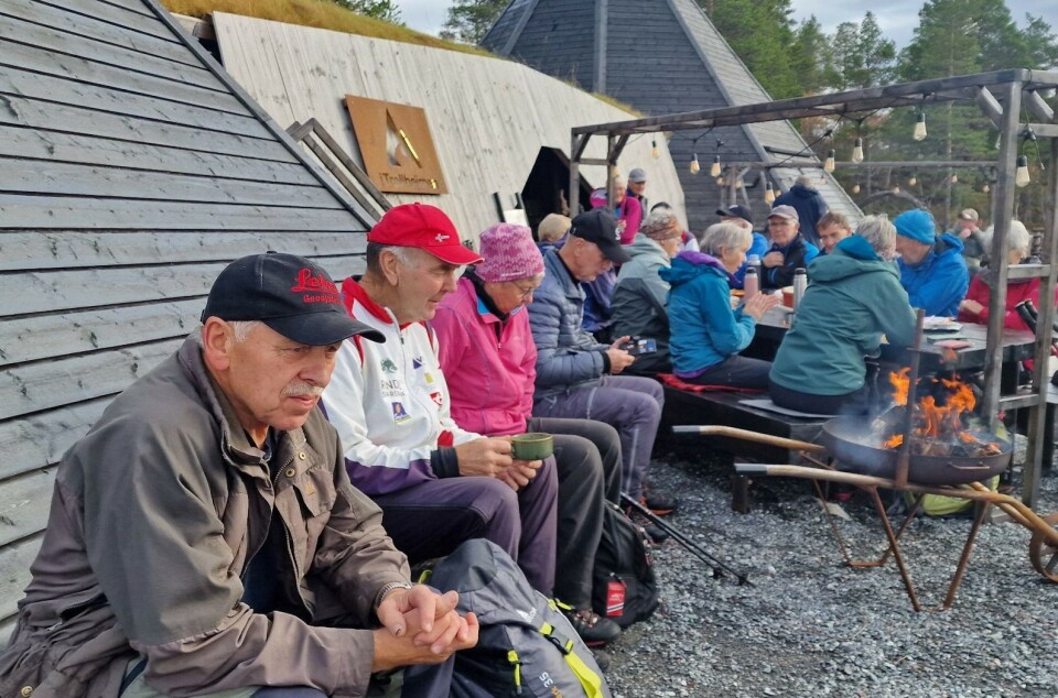 Tirsdagstur til Trollheimstunet -sesongavslutning Mange turkledde folk som sitter og drikker kaffe foran en trebygning med to lavvoer av tre.