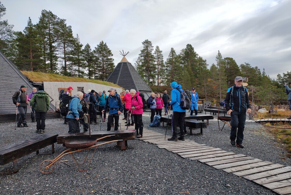 Tirsdagstur til Trollheimstunet -sesongavslutning Mange turkledde folk foran en trebygning med to lavvoer av tre.