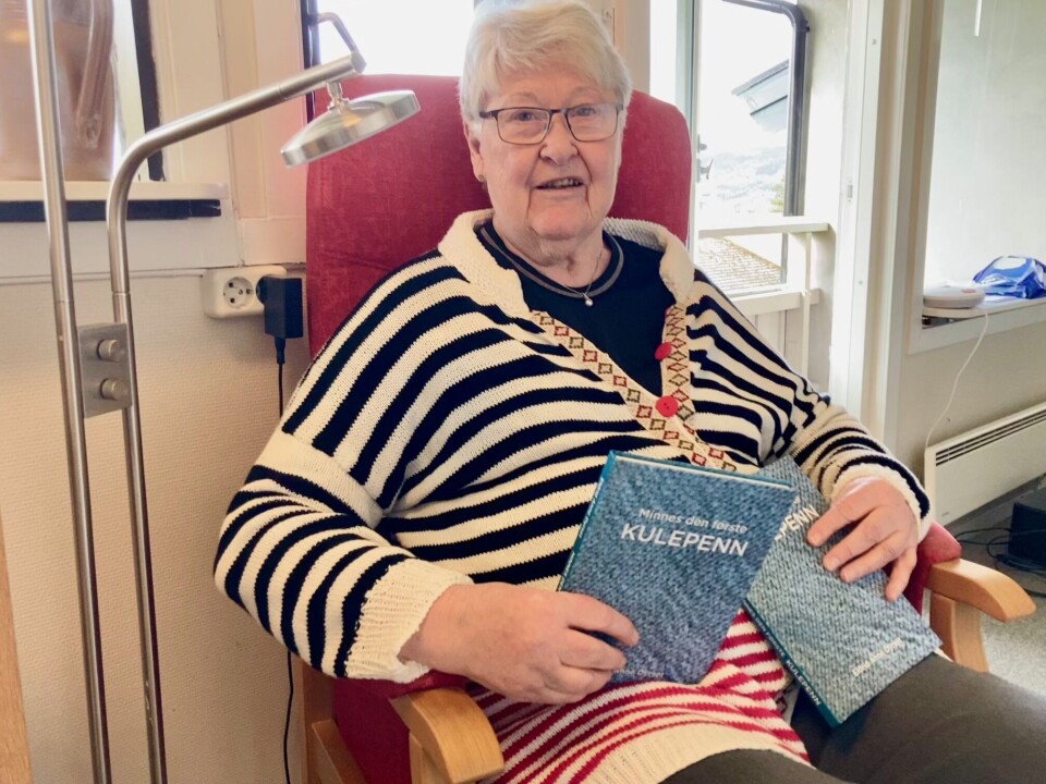 Eldrid Anne Dyrset gir ut bok med småstykker, dikt og novelle. Eldre dame i rød stol med bok i hånda.