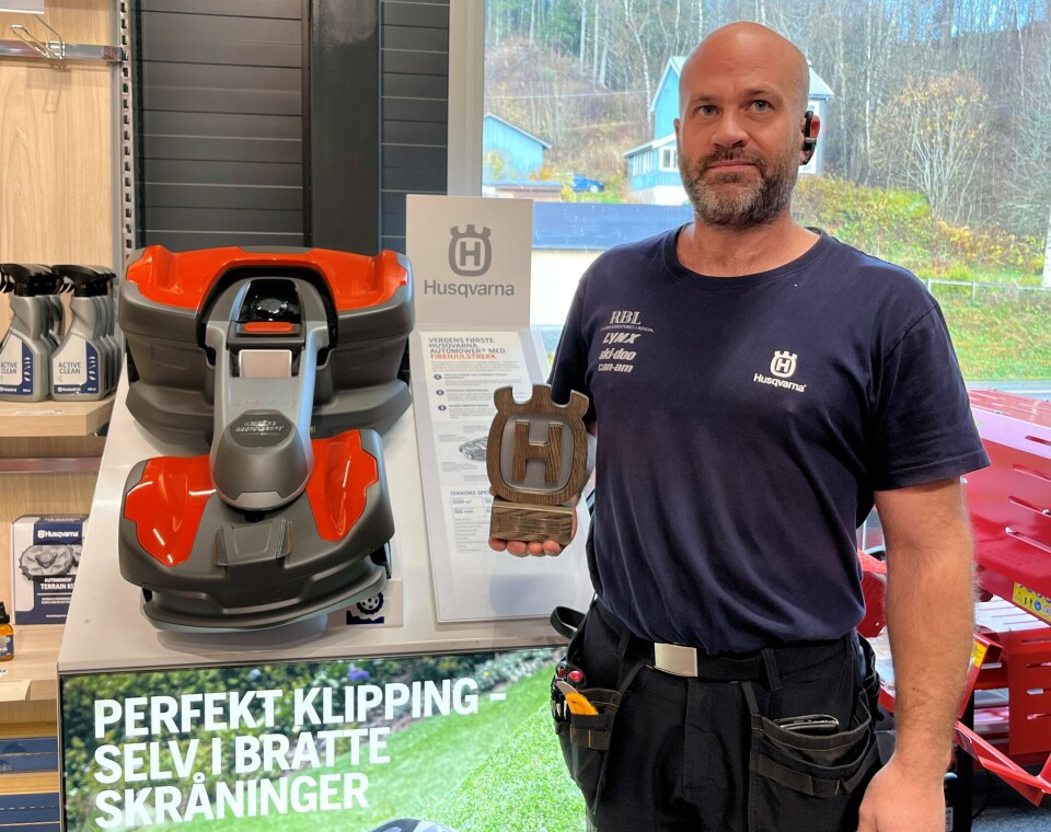 Steffen Møkkelgård med utmerkelsen for flest leasingkontrakter av Automower i Norge i år. En mann som står ved siden av en robotplenklipper inne i en butikk.