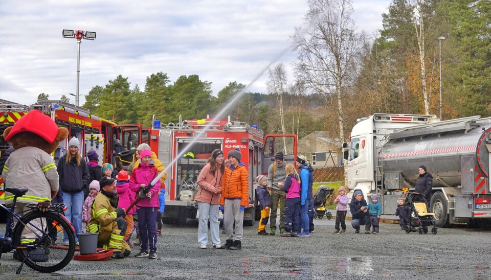 Den som ville, fikk teste å treffe tre bokser som mål med vannet fra en ordentlig brannslange. Jente spyler vann mens mange ser på. Ny og gammel brannbil i bakgrunnen i tillegg til tankbilen.