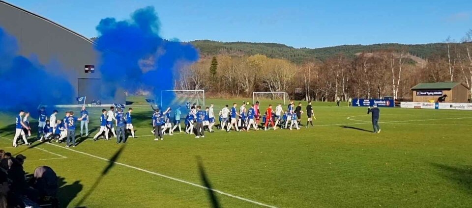 God stemning før avspark på Syltøran. To fotballag går på banen med blå røyk rundt seg