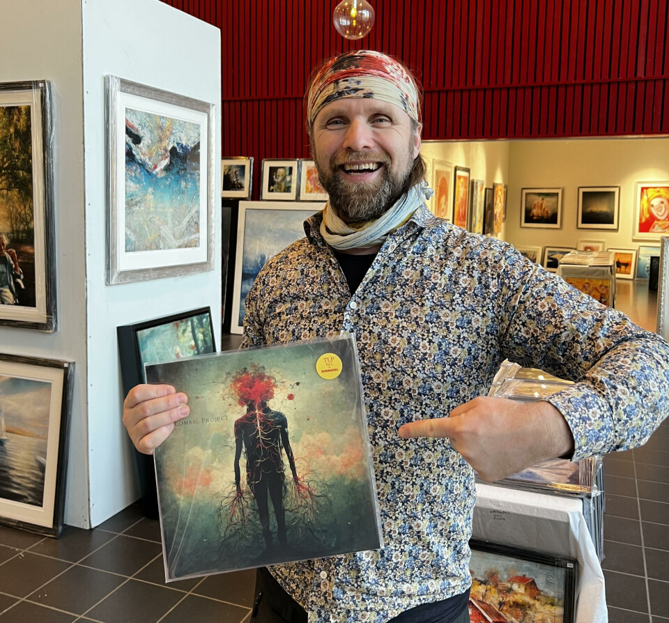 Frank fikk lyst til å gi bort et album til Aune Sand, positiviteten selv. En mann i blomstrete skjorte står med en LP plate i hånden. Bak han er det flere malerier