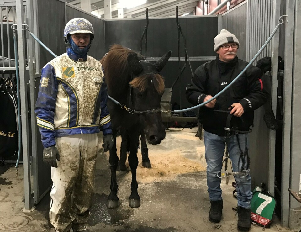 Madonna J.L, kusk Atle Eggan og eier Jon Fiske. En travkusk med sølete drakt, en annen mann og en hest i en oppselingsboks.