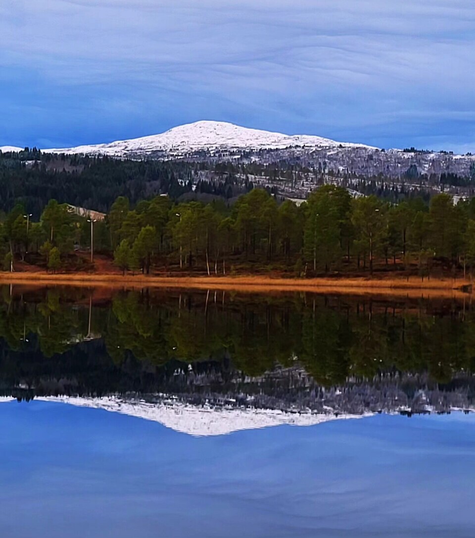 Igltjønna 29. oktober. Et fjell med snø på toppen speiler seg i et vann.