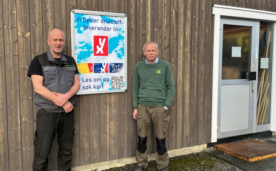 Olav Morten Tørset og Morten Halgunset vil fortsette å drive bensinstasjonen på samme vis som tidligere, bare med ny drivstoffleverandør. To menn ved en husvegg, med en plakat mellom seg.