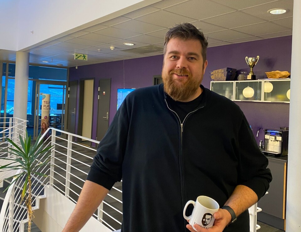 Espen Røv, operasjonell leder i Svorka ser frem til å få ansatt enda en drifts- og servicekoordinator – og håper mange søker før fristen 22. november. En smilende mann, innendørs, med en kaffekopp i handa.