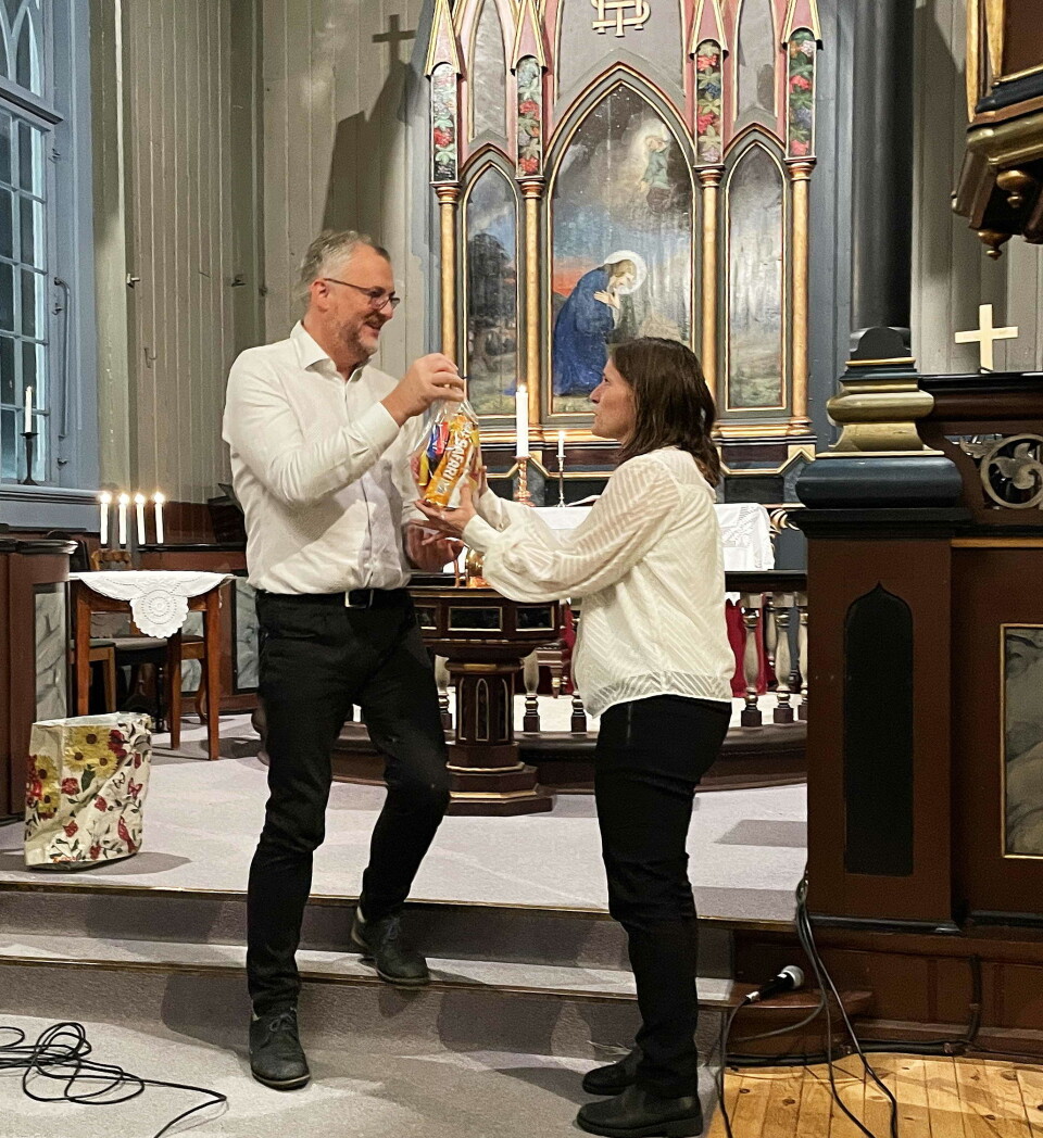 Tor Rune med godord og godtepose til kveldens altmulegkvinne Bodil Kvam Aasbø. En mann som overrekker en pose til ei dame. I bakgrunnen ei altertavle i ei kirke.