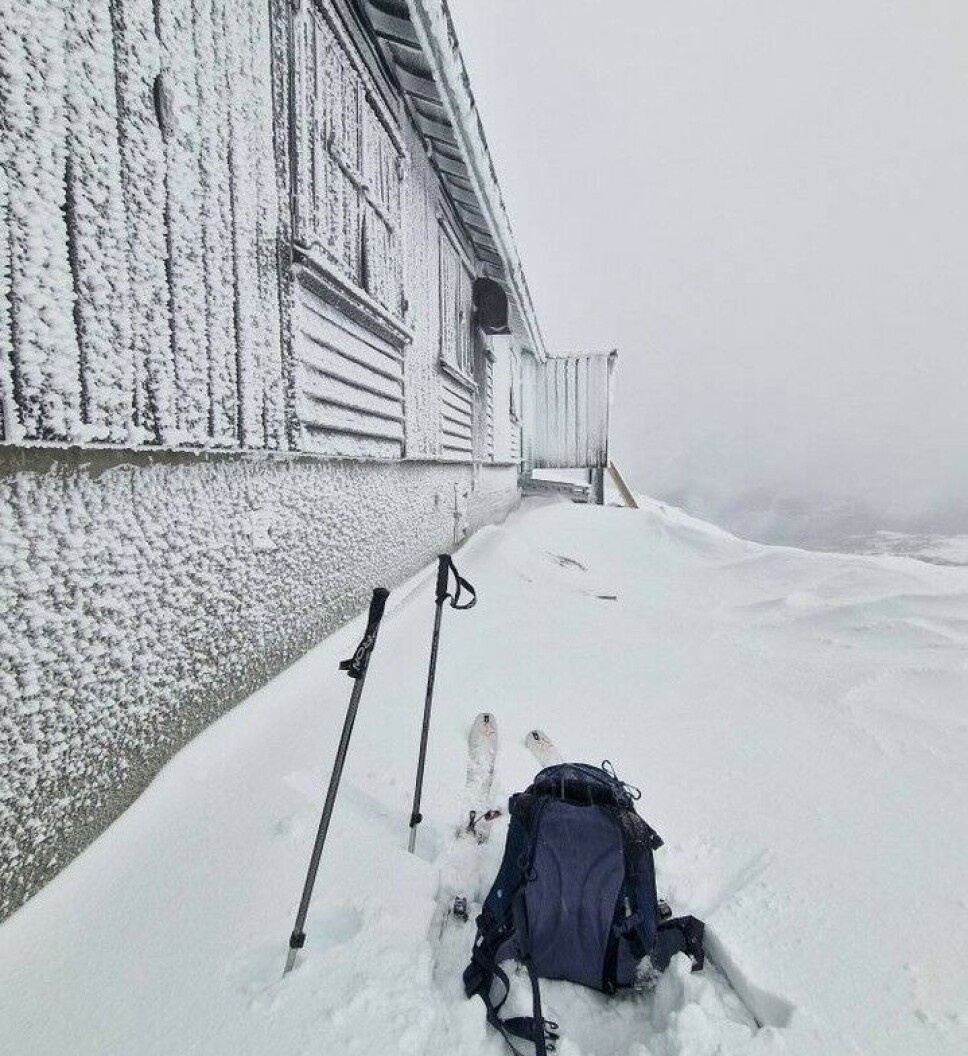 Strengentrasèen. En sekk og et par skistaver som står foran en snødekt husvegg.