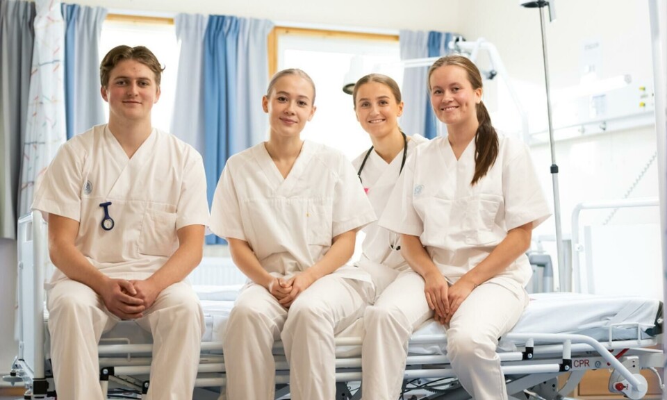 Har du lyst til å utdanne deg til sjukepleiar der du bur? Tre unge damer og en ung mann, alle i helseuniformer, som sitter på ei seng inne på et sykehusrom.