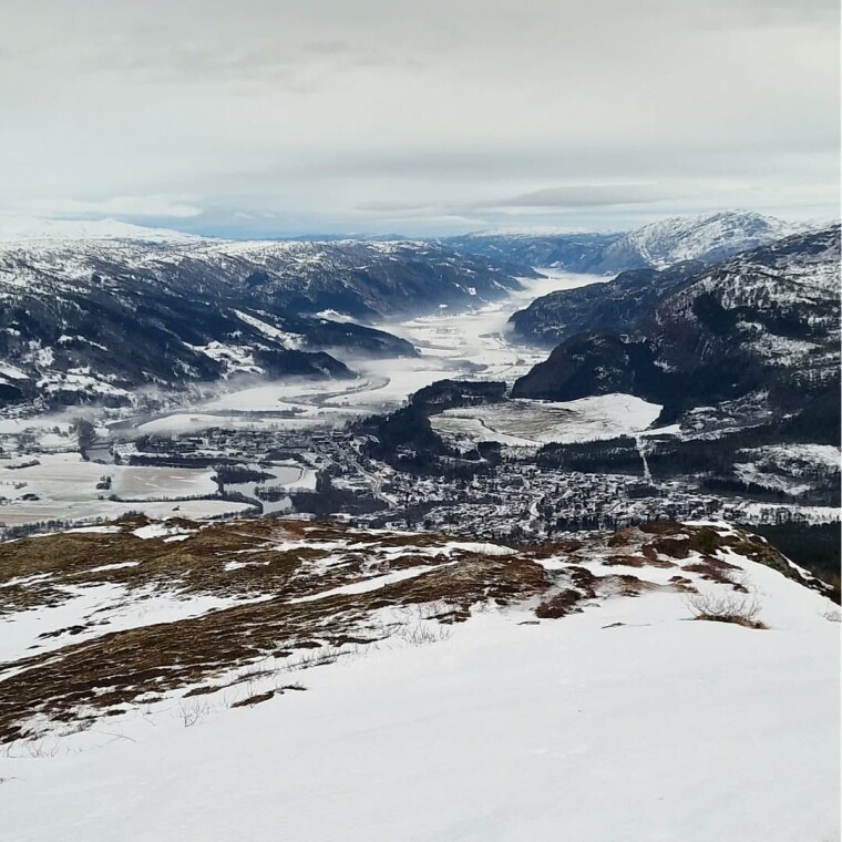 God morgen 14. desember Utsikt ned mot en fjord fra en fjelltopp. Delvis snødekt landskap.