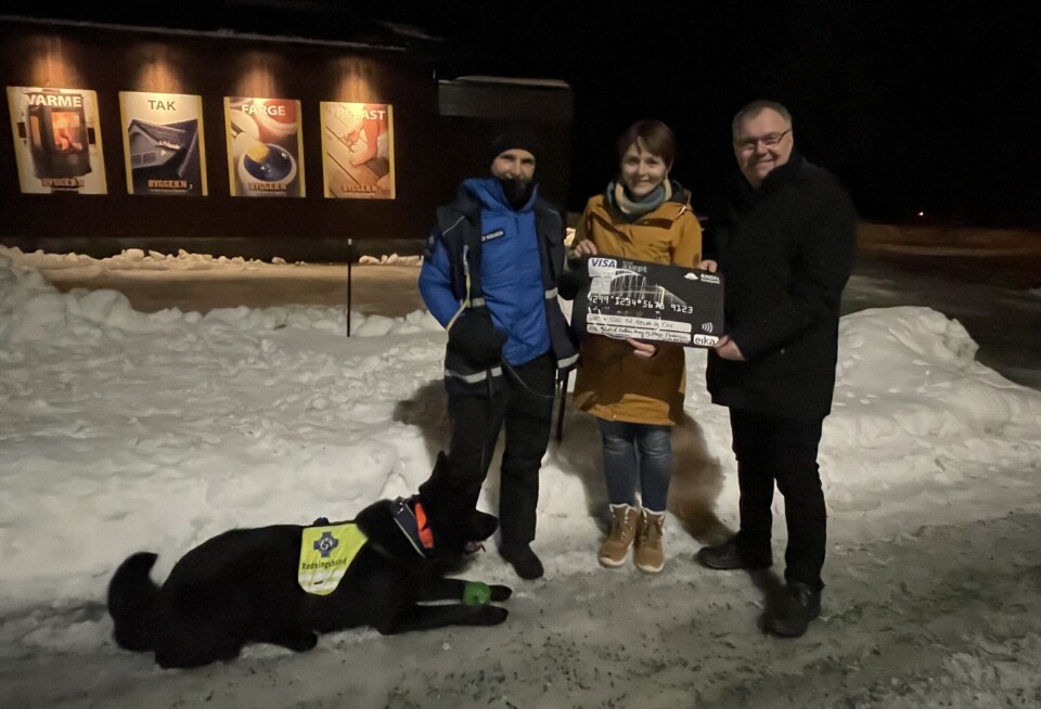 Cox og Heidi Solheim får overlevert 10000 kr for jobben de gjør for vår sikkerhet. en svart hund til venstre, en blåkledd dame ved siden av, til høyre for den en brunkledd dame med en sjekk i hånden. Til høyre en mann. Holder også i sjekken