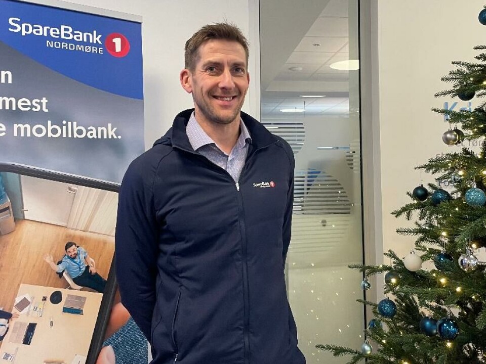 Olav Magne Dønnem på jobb i Sparebank 1 Nordmøre sin avdeling i Kristiansund like før jul. Mann foran reklame for SpareBank 1 Nordmøre og ved siden av et pyntet juletre.