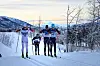 Løper i hvit Rindal Il-drakt ser bort på 3 mørkkledde løpere i det andre skisporet.