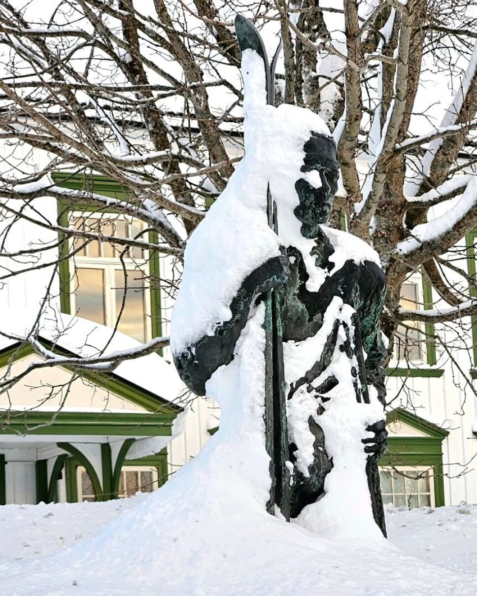 En nedsnødd skiløper. En statue delvis begravd i snø.