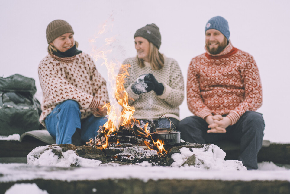 Nå finner du bålplasser i turplanleggeren UT. Tre personer som sitter ved et bål i snøen.