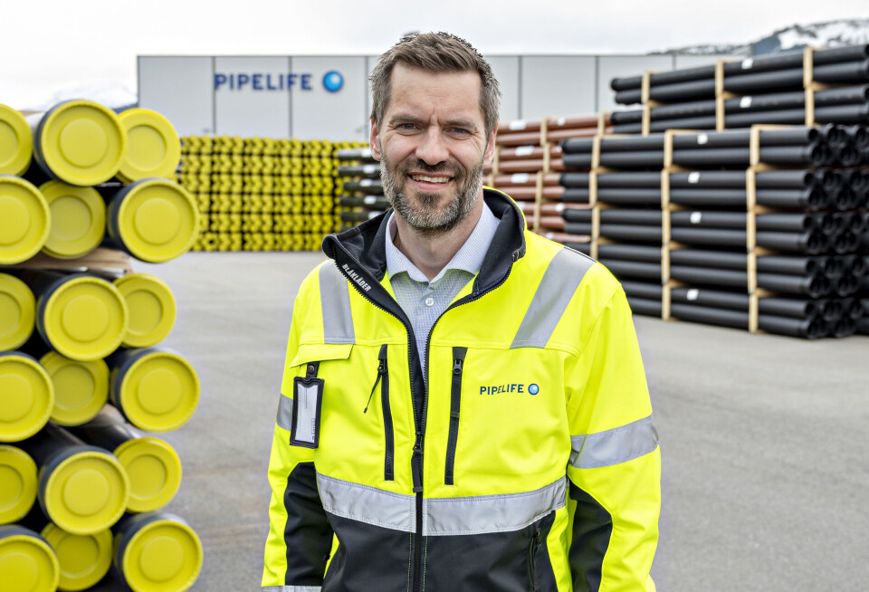 Sigmund Aandstad. En mann med flere stabler med rør og et fabrikkbygg bak seg.