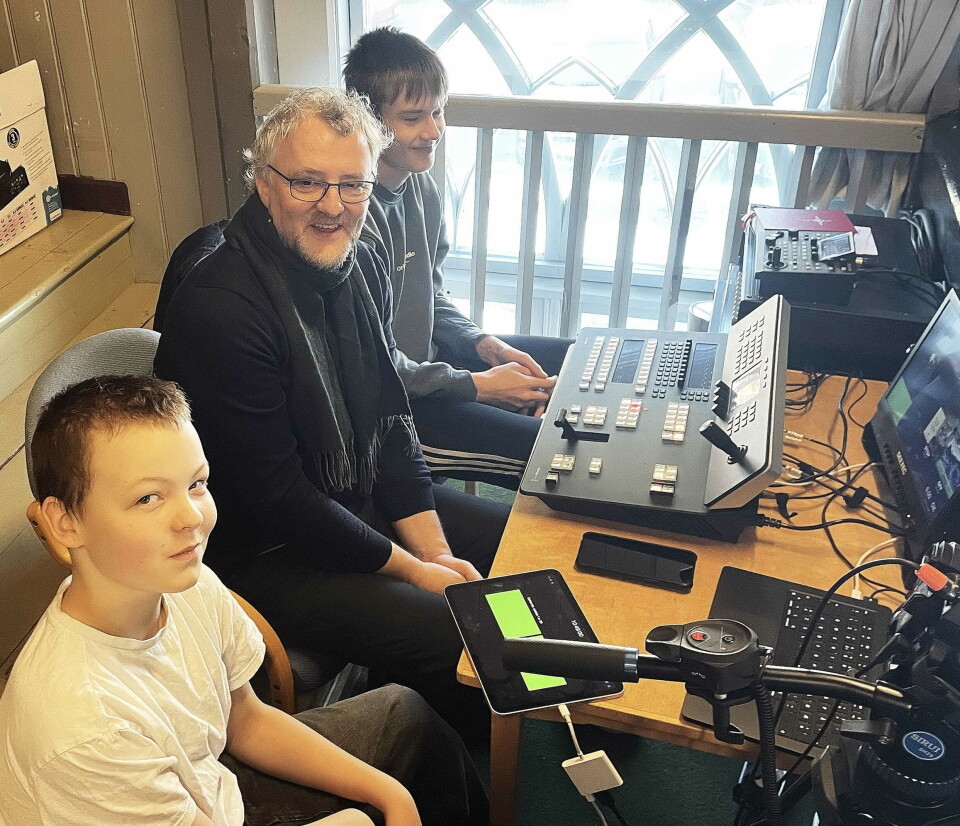 TV-teamet på galleriet: Kyrkja sin altmulegmann Tor Rune Halset med konfirmantane Levion (nærast) og Varg – som sørga for at salmetekstene kom ut på nettet. En mann og to unge gutter som sitter med teknisk utstyr foran seg.