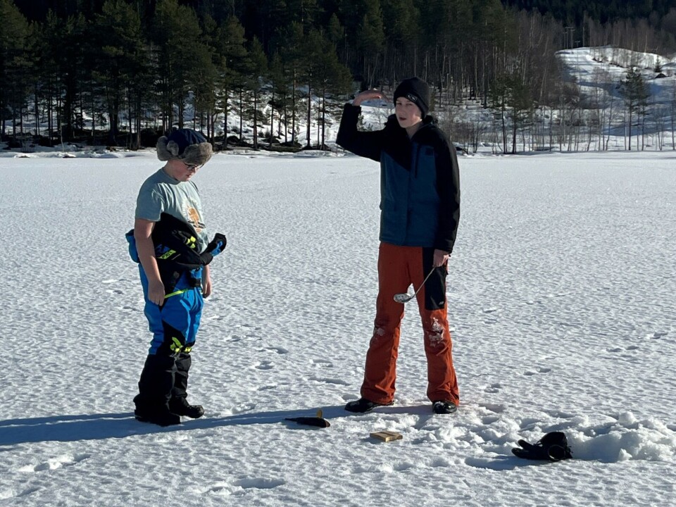 Det var snøre ut i flere hull på isen, og her har de dratt opp enda en fisk. To gutter som fisker på isen.