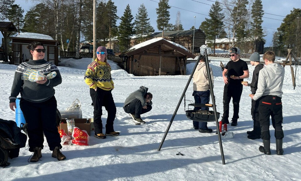 Grilling av pølser på bålpanne. Flere personer rundt ei bålpanne i snøen.