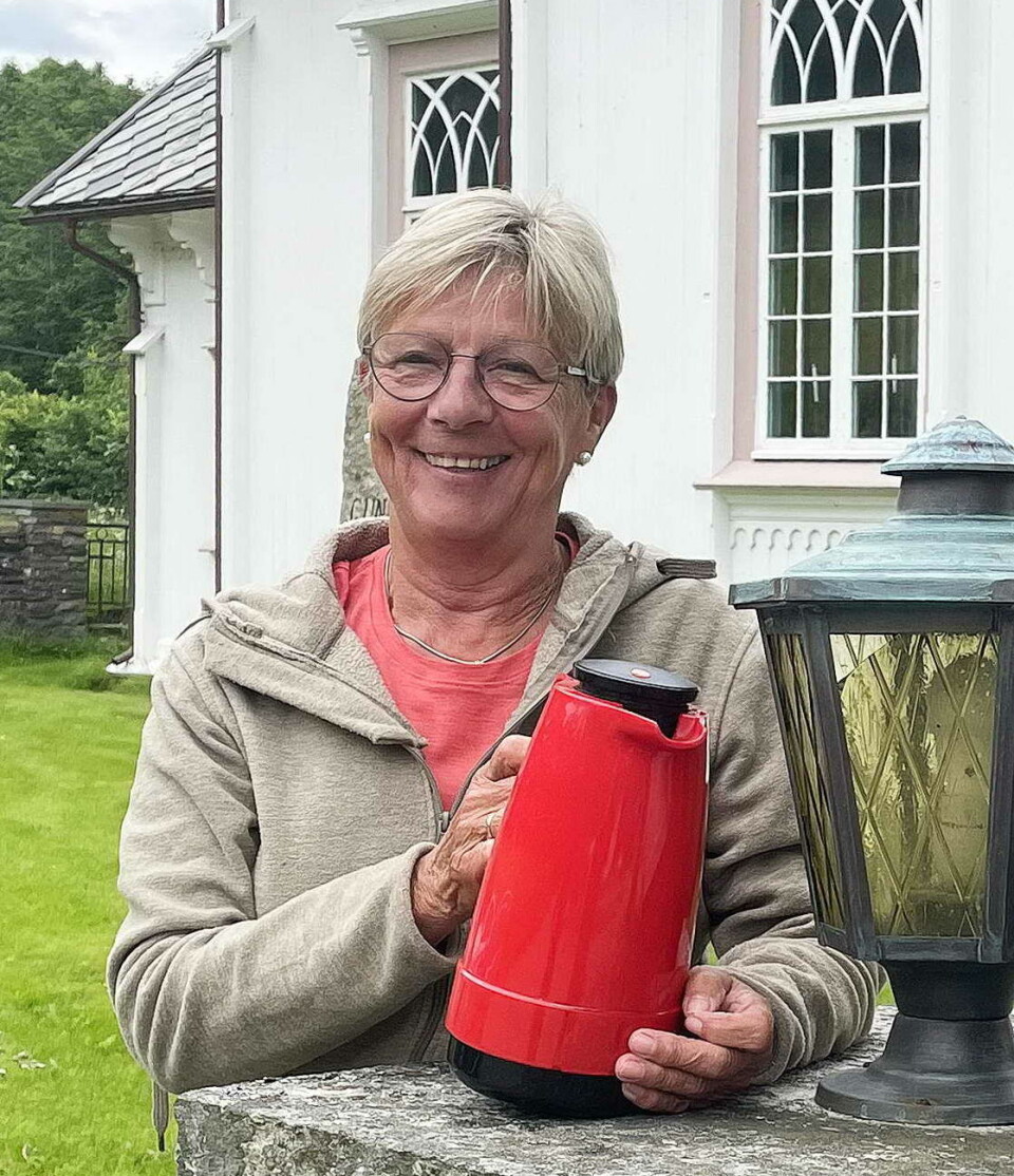 Som ofte før inviterer soknerådsleiar Eva til treff og servering. Ei smilende dame med innsamlingsbøsse foran ei kirke.