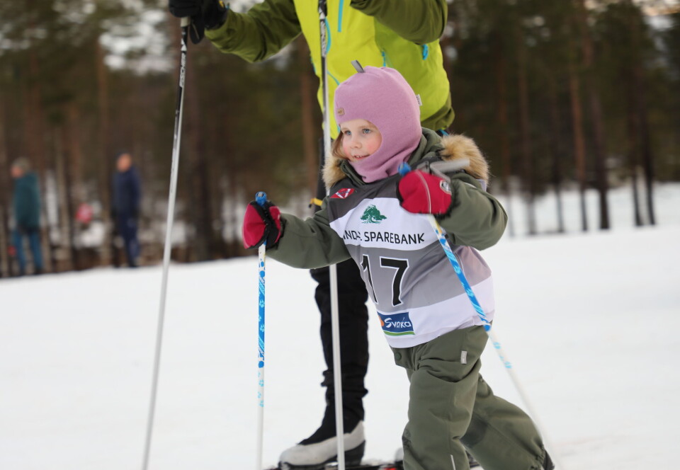 Et barn som går på ski, med en voksen ved siden av.