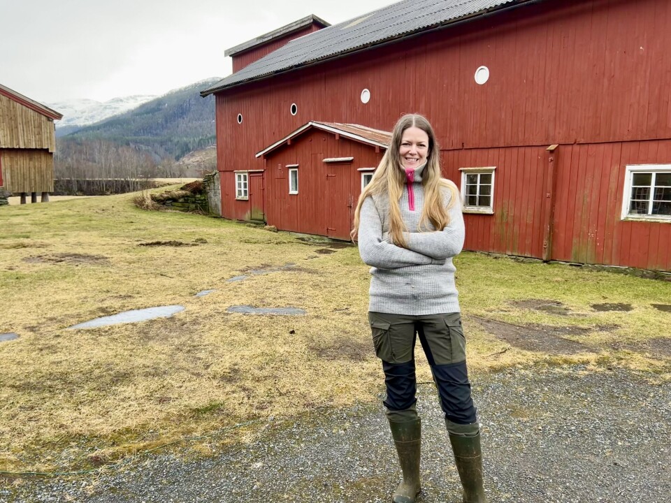 Stine Grytskog Ramsøy trives godt som bonde, og håper å kunne leve av å selge produkter fra gården. Dame med langt hår foran et gammel rødmalt fjøs.