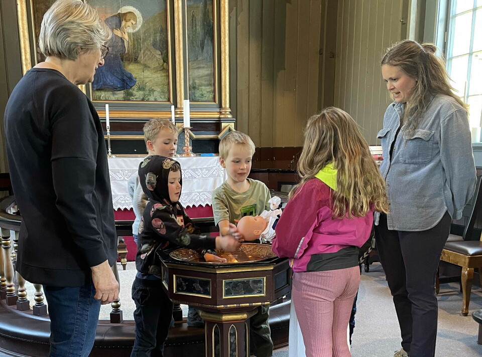 Dokka vart skikkeleg døypt. Namneforslaga var mange, og kva dei landa på, hugsar ikkje fotografen ... Barn som døper ei dokke i ei kirke.