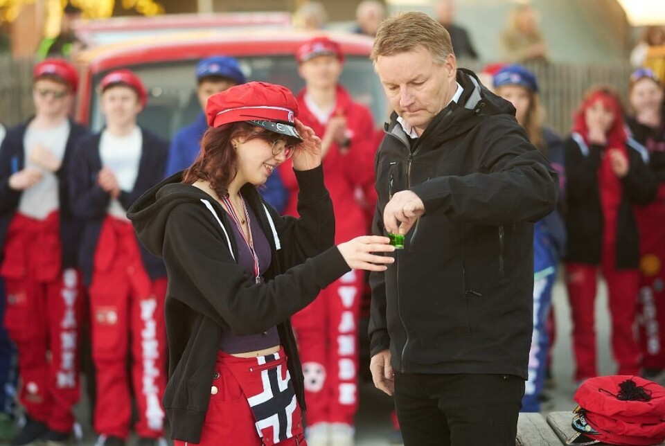 Fiske delte ut drikke etter lua var satt på plass. Mann serverer russ. Mange russ og en russebil i bakgrunnen.