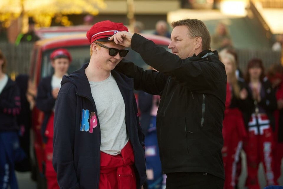 'Fiske prest' hadde kontroll på hvem som skulle ha hvilken lue. Mann tar på en russelue på en russ. Russ og russebil i bakgrunnen.
