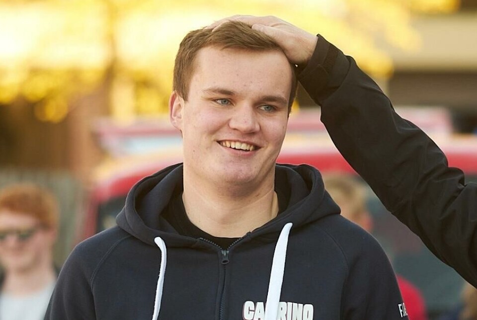 Russepresident Jørgen Lundemo Solli. En hånd på hodet til en russ. Russ og russebil i bakgrunnen.