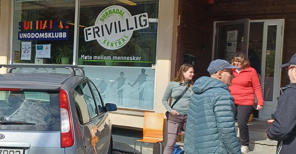 Frivilligsentralen på Skei. Mennesker foran ei inngangsdør. Frivilligsentralens logo på vinduet.
