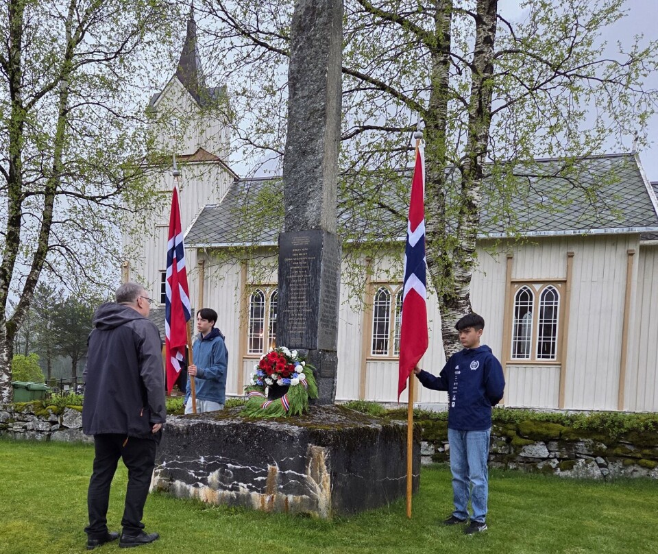 Ordførar Hugo Pedersen la på krans ved «soldatbautaen» ved Todalen kyrkje. En mann foran et minnesmerke ved ei kirke, der det er lagt ned en krans. To unge gutter står ved minnesmerket og holder hvert sitt norske flagg.
