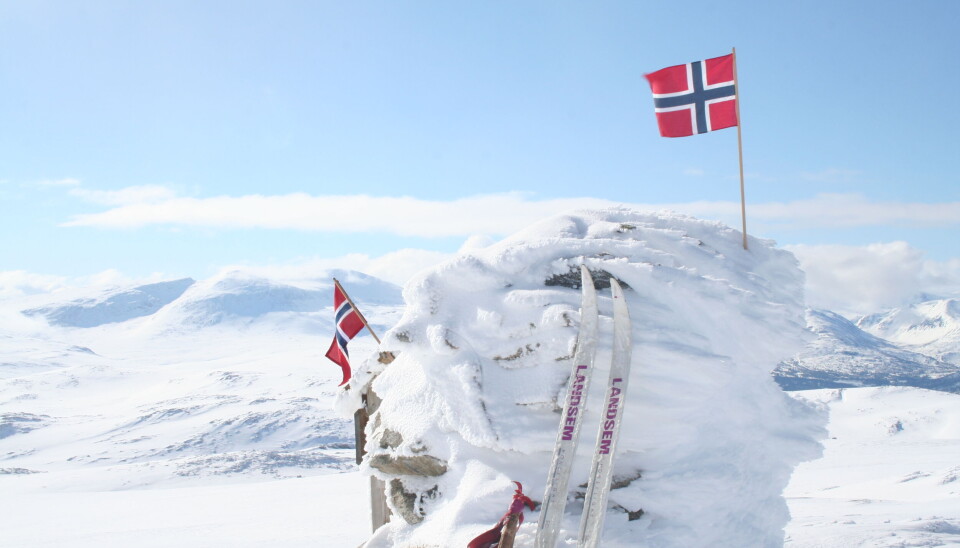 Trollhetta sett fra Urvarden. To norske flagg på en varde på det snødekt fjell, og et skipar lent opp mot varden.